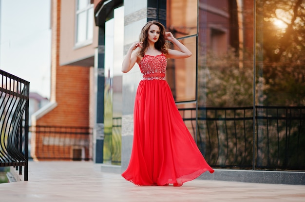 O retrato da menina na moda no vestido vermelho colocou a janela do espelho de fundo do edifício moderno ao pôr do sol