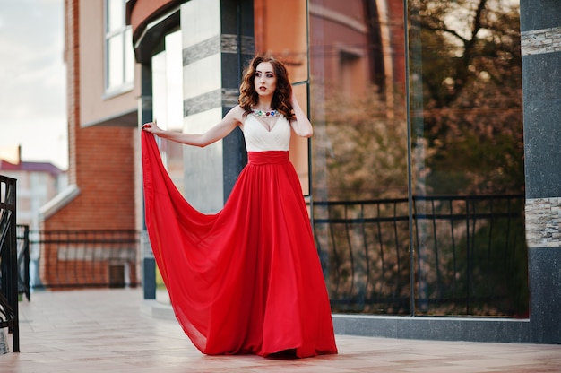 O retrato da menina na moda no vestido vermelho levantou a janela do espelho de fundo do edifício moderno