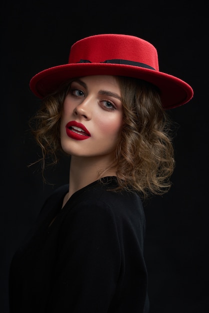 O retrato da moça bonita, batendo o batom vermelho, dia compõe e chapéu vermelho elegante.