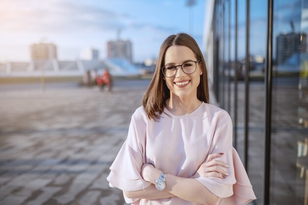 O retrato da morena de sorriso lindo vestiu a posição elegante com os braços cruzados no telhado