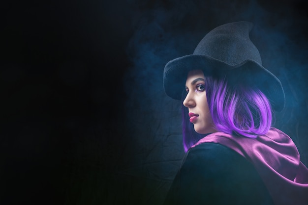 O retrato da mulher no traje de halloween com brilhante compõe e cabelo roxo nas sombras em um preto.