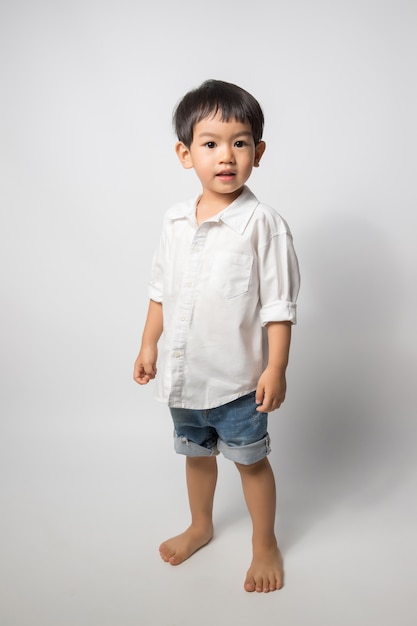 O retrato de 2 anos do menino idoso veste a camisa branca e o short brim no fundo branco.