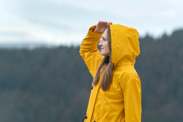 O retrato de uma jovem de casaco amarelo na natureza olha para a distância Floresta ao fundo Vista lateral