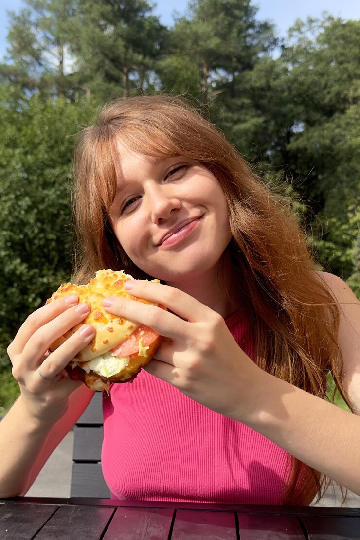 Foto o retrato de uma jovem feliz está comendo um hambúrguer delicioso e suculento do lado de fora do café olhando para a câmera