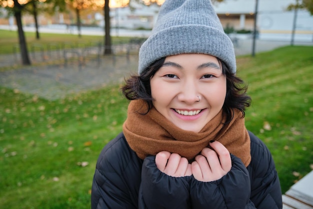 O retrato de uma linda garota asiática de chapéu e cachecol anda pela cidade em um clima frio de primavera sorri e l