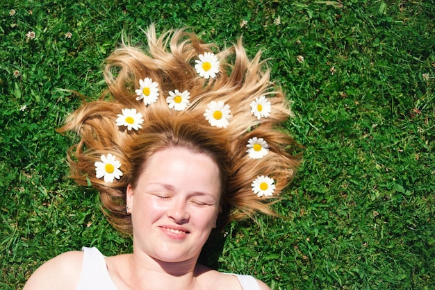 O retrato de uma linda mulher com os olhos fechados deitada no campo com flores de camomila no cabelo