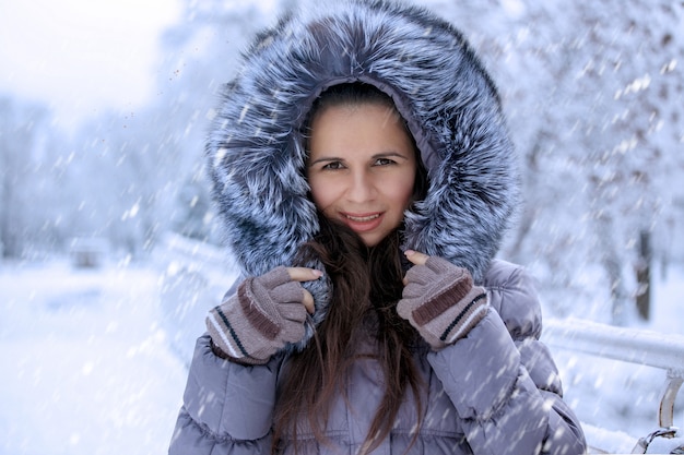 O retrato de uma mulher bonita do inverno no chapéu forrado a pele está andando no parque