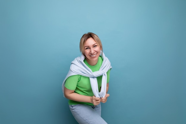 O retrato de uma mulher loira e alegre e sorridente em uma roupa casual sorri amplamente em um azul