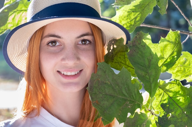 O retrato do adolescente consideravelmente novo com cabelo vermelho no chapéu amarelo perto da árvore verde sae.