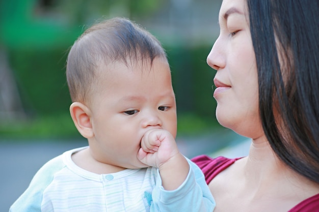 O retrato do bebê infantil está sugando a mão com levar asiático da mãe.