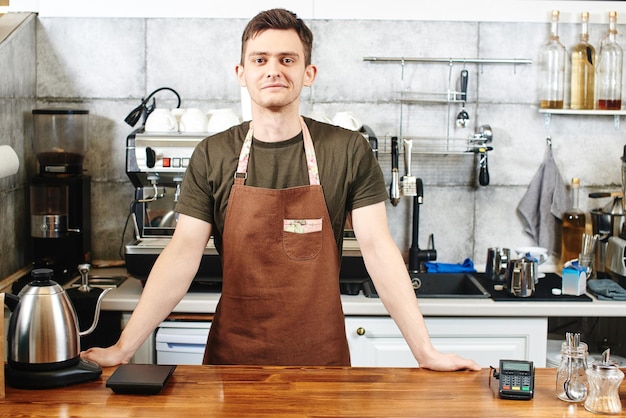 O retrato do cara baristas no local de trabalho no fundo do café