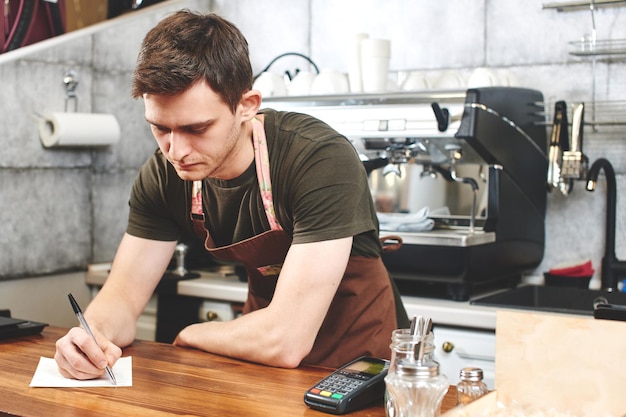 O retrato do cara baristas no local de trabalho no fundo do café