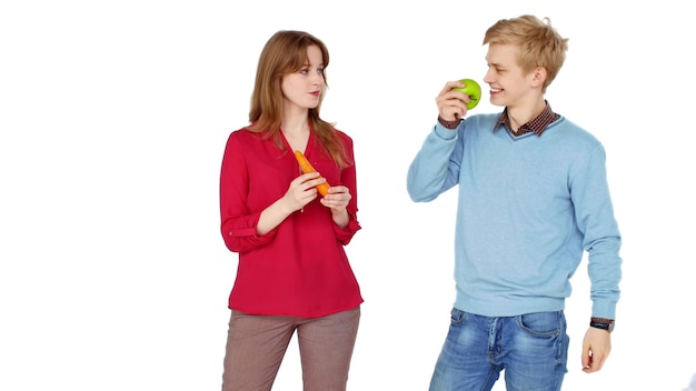 O retrato do casal jovem feliz come maçã fresca e cenoura isolada no fundo branco
