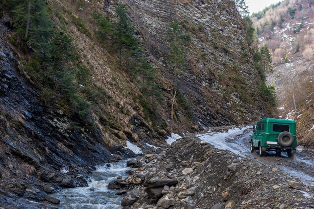 O riacho da montanha entre rochas perto de um carro velho está passando pela estrada na floresta