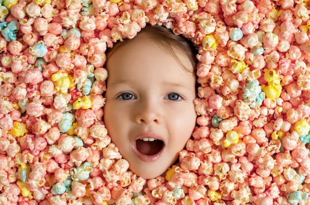 O rosto da criança está rodeado por uma grande quantidade de pipocas doces coloridas