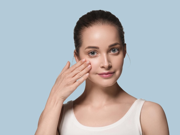 O rosto de mulher de pele limpa natural compõe um belo modelo de beleza. Cor de fundo. Azul.