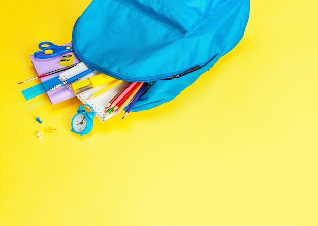 O saco da escola. Mochila com material para a escola em fundo amarelo. Copie o espaço para o texto.