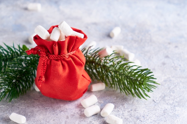 O saco vermelho do Natal com marshmallows doces e abeto ramifica no conceito claro do fundo, do Natal e do ano novo. Copie o espaço