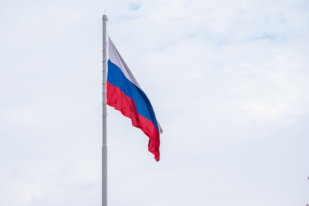 Foto o símbolo estatal da federação russa ao vento uma grande bandeira russa contra um céu azul com nuvens em close