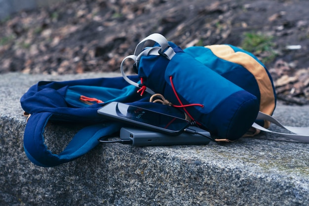 O smartphone é carregado com um carregador portátil. Power Bank carrega o telefone ao ar livre com uma mochila para turismo na natureza.