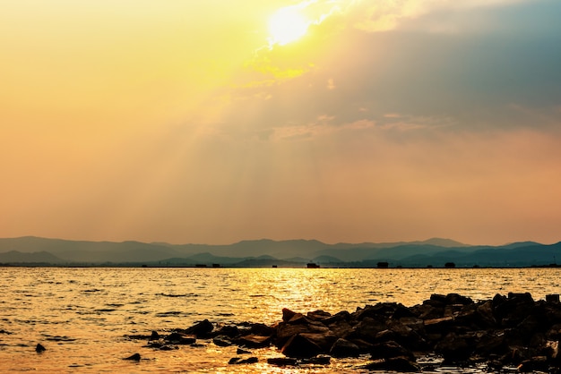 O sol da bela paisagem da natureza brilha dourado na nuvem refletindo a luz amarela na pilha de rocha do céu na água de um lago tropical ao fundo da montanha na Represa de Krasiao, Suphan Buri, Tailândia