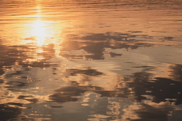 O sol e as nuvens de fundo natural se refletem na água ao pôr do sol no verão