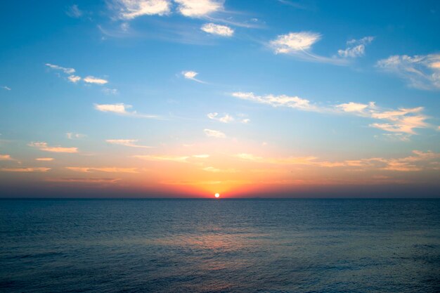 O sol está se pondo sobre o oceano e o céu está azul.
