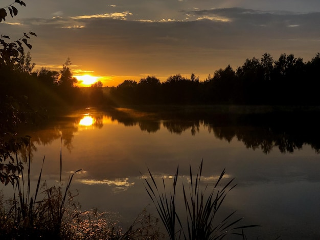 O sol se põe no horizonte acima do lago calmo na paisagem natural da noite de verão