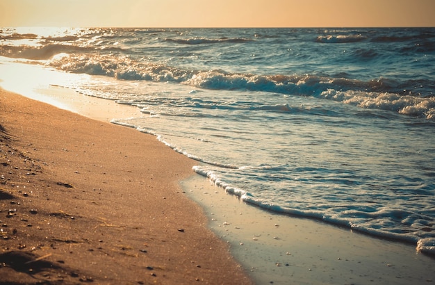 O sol se reflete nas ondas que rolam na praia de areia, close-up