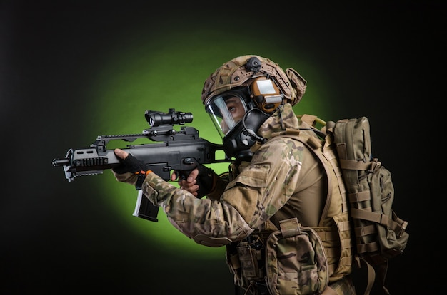 O soldado masculino em roupas militares com uma arma em um fundo escuro com uma máscara de gás