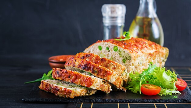 O solo caseiro saboroso cozeu o bolo de galinha com ervilhas verdes e brócolis na tabela preta. pão de carne americana de alimentos.