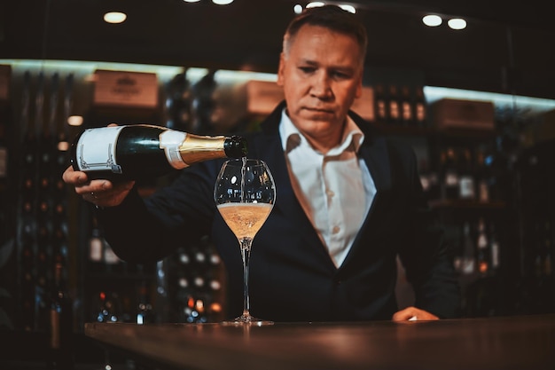 O sommelier de vinho elegante e arrumado está colocando vinho branco no copo para prová-lo.