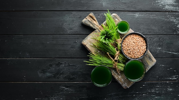 O suco do trigo germinado verde e grãos de trigo Em um fundo preto Micro Verde Comida saudável Vista superior Espaço livre para o seu texto