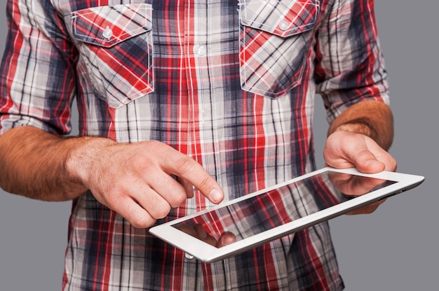 O tablet é tão funcional! Foto de close-up de um homem usando seu tablet em pé contra um fundo cinza