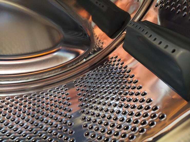 Foto o tambor da máquina de lavar por dentro tanque de metal brilhante com orifícios e protuberâncias superfície de aço inoxidável com orifícios feitos de chapa de aço inoxidável vista interior de uma máquina de lavar
