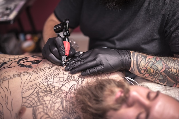 O tatuador faz uma tatuagem na pele de seu cliente no estúdio de tatuagem./Especialista em tatuagens faz tatuagens no salão.