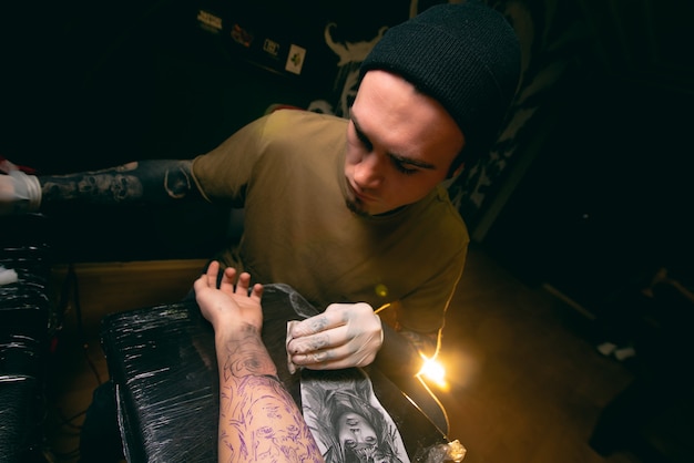 O tatuador profissional faz uma tatuagem no close da mão do cliente