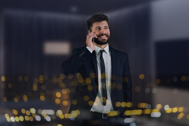 Foto o telefone do homem perto da janela com as luzes da cidade