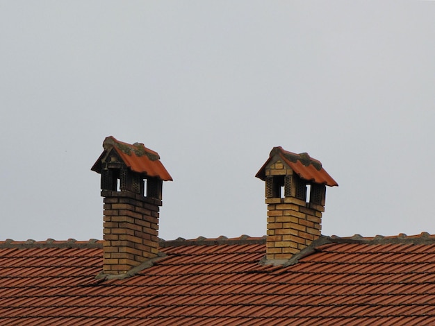 O telhado da casa com telhas e duas chaminés da casa de tijolo no fundo do céu