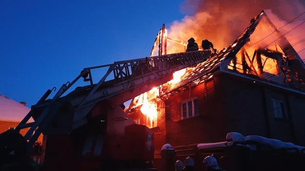 O telhado da casa está pegando fogo O prédio residencial queima a vila Os bombeiros apagam um incêndio do guindaste de cima Fumaça e faíscas