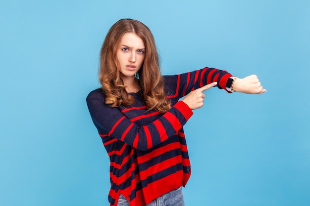 O tempo se foi Jovem mulher séria vestindo suéter listrado estilo casual mostrando o tempo em seu relógio olhando para a câmera com expressão mandona