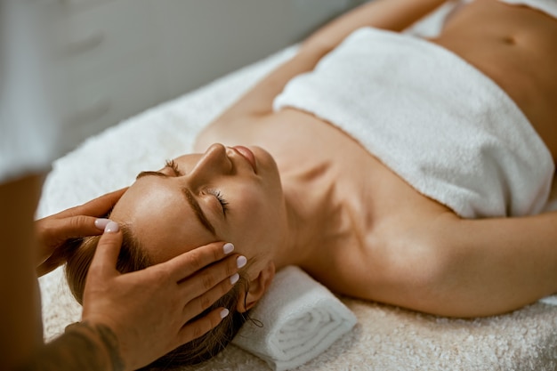 O terapeuta está fazendo uma massagem relaxante facial para uma jovem em um moderno gabinete de bem-estar
