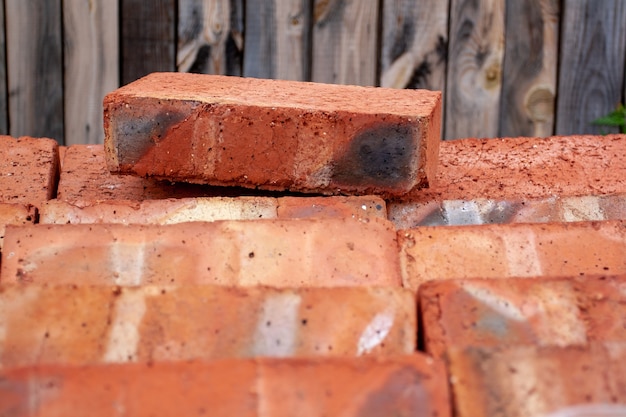 O tijolo vermelho Fireclay encontra-se em uma palete de tijolos contra o fundo das placas. Foco seletivo no tijolo. Imagem horizontal.