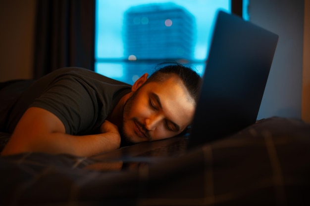 Foto o tipo dorme na cama enquanto trabalha no portátil em casa.