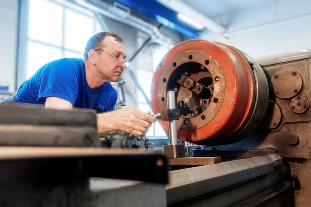 O torneiro de metal idoso trabalha na oficina atrás do torno Fluxo de trabalho autêntico Trabalhador real