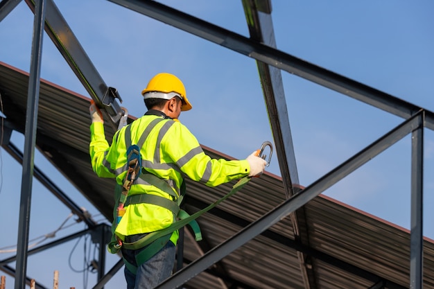 O trabalhador da construção de telhado asiático usa equipamento de segurança de altura para instalar a estrutura do telhado. dispositivo antiqueda para trabalhador com ganchos para cinto de segurança no canteiro de obras.