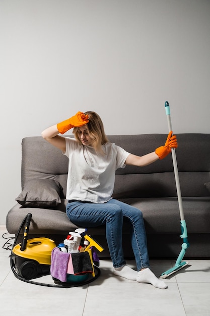 O trabalhador do serviço de limpeza está cansado e faz uma pausa depois de lavar o chão, desinfetar a vapor e limpar a cozinha com detergente O limpador de menina cansada está descansando no sofá