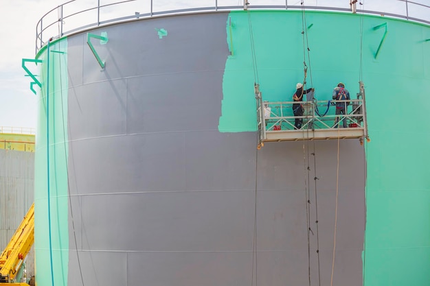 O trabalhador do sexo masculino leva o teleférico segurando uma escova de pintura industrial usada para a superfície da superfície do óleo do tanque da placa de concha cor verde