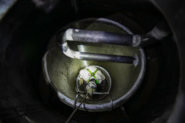 O trabalhador masculino de vista superior sobe as escadas para a área de graxa química de carbono do tanque confinada