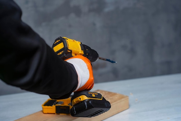 O trabalhador masculino segura uma chave de fenda elétrica sem fio em suas mãos contra o fundo de uma ferramenta de construção e uma parede de concreto